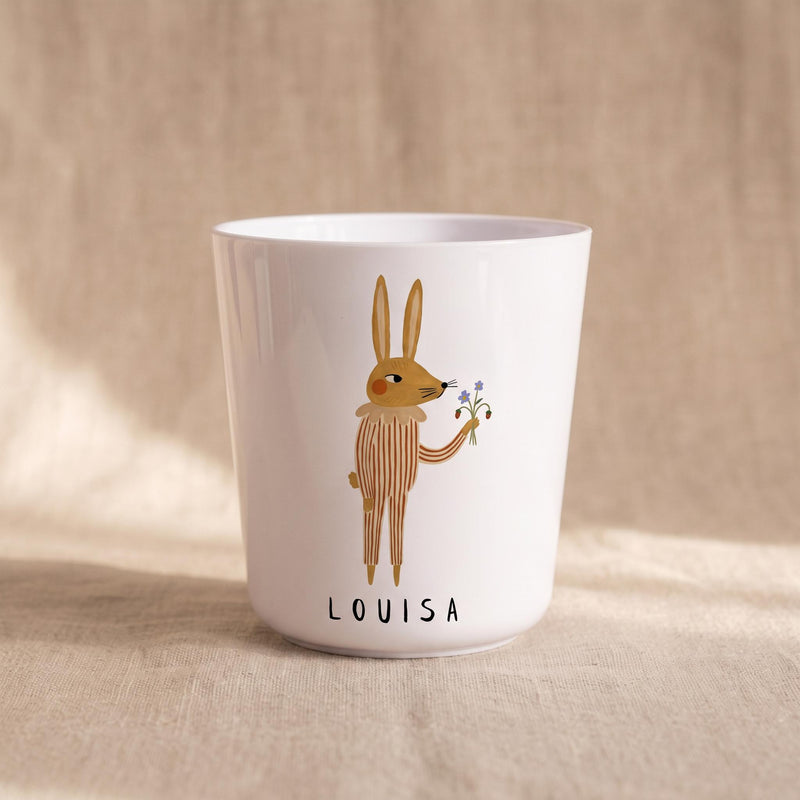 A white polymer cup with an illustration of a brown rabbit holding small flowers and the name Louisa printed underneath.