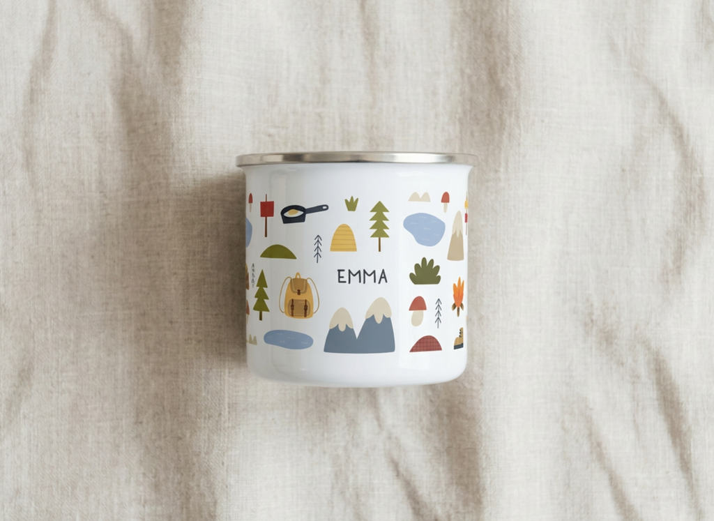 Personalised Kids Camping enamel mug with the name EMMA among small mountains, tents, trees and a campervan, on beige linen.