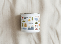 Personalised Kids Camping enamel mug with the name EMMA among small mountains, tents, trees and a campervan, on beige linen.