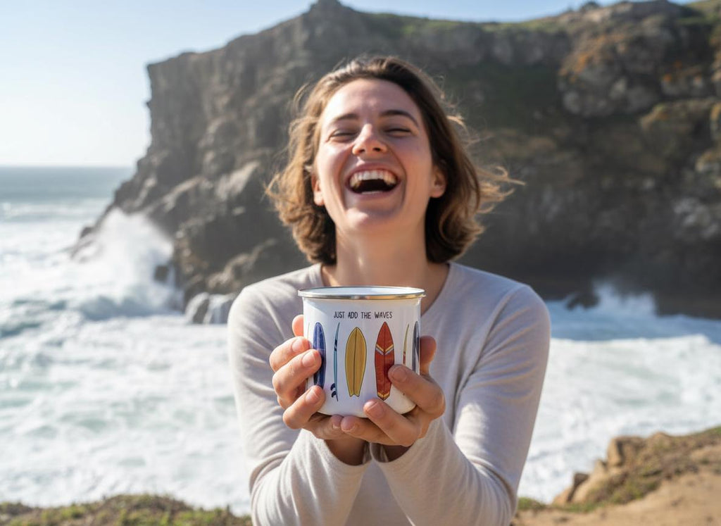 A white enamel mug featuring a colourful graphic print of various surfboards and the text "JUST ADD THE WAVES" printed in black lettering near the top rim. The mug has a metallic silver rim and a smooth, cylindrical body design.
