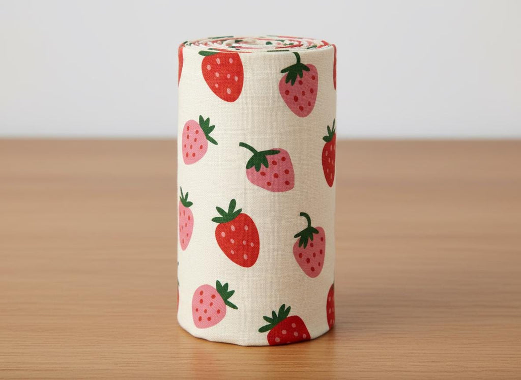 A cylindrical roll of off-white fabric featuring a repeating pattern of red and pink strawberries with green stems. The strawberries are scattered across the surface of the fabric roll in a simple, uniform, and repeating graphic design.