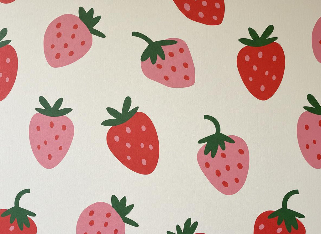 A repeating pattern on a light cream background featuring stylised strawberries in shades of bright red and soft pink. Each strawberry includes a dark green leafy stem at the top and small dots representing seeds across the fruit surface.