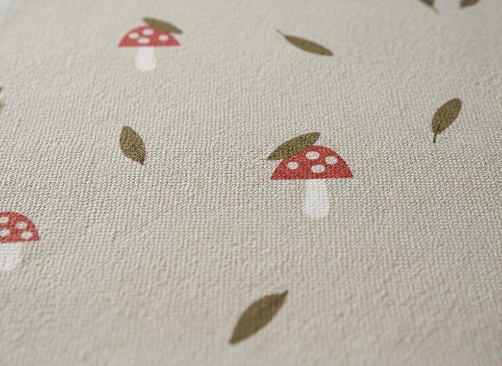 Close-up of a beige fabric featuring a repeating pattern of red mushrooms with white spots and brown leaves. The fabric has a textured appearance, possibly linen or cotton.
