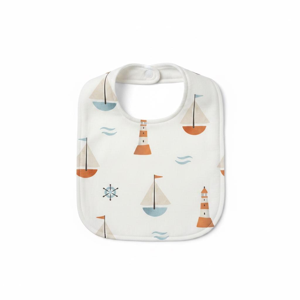 A white baby bib featuring a repeating pattern of sailboats, lighthouses, ship wheels, and small waves in shades of muted orange, light blue, and dark grey. The bib has a rounded shape with a snap closure at the top neck opening.