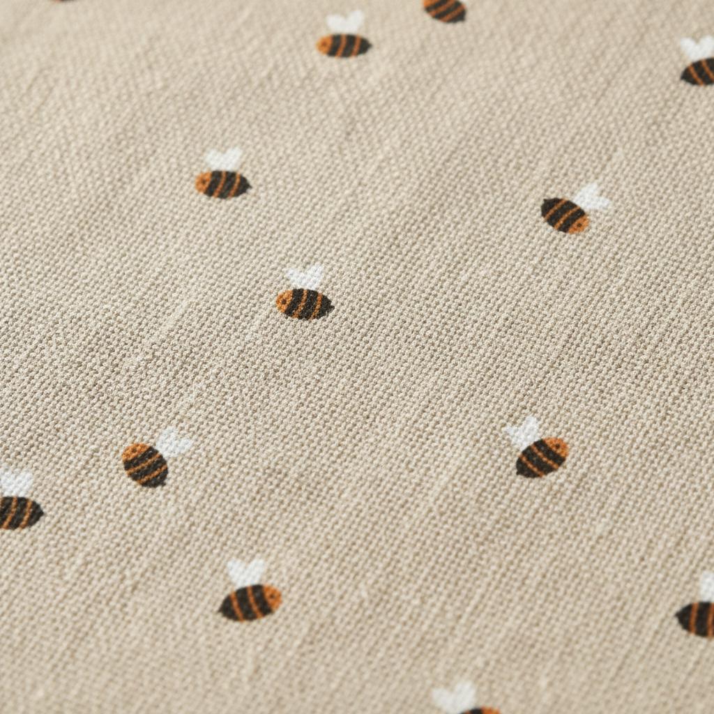 A light beige fabric with a repeating pattern of small, embroidered bees. Each bee features brown and black horizontal stripes on the body and two small white wings. The textile has a visible woven texture throughout the surface.