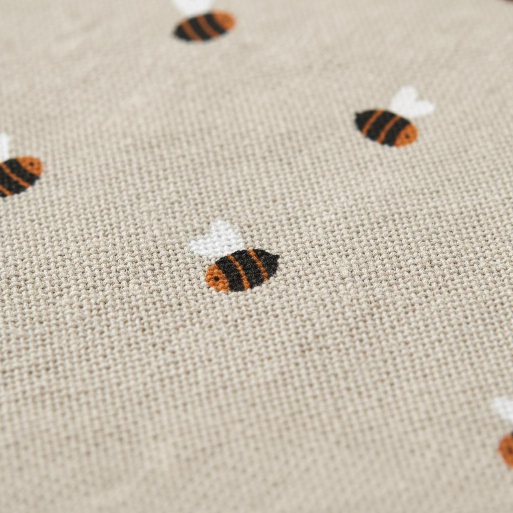 A light beige fabric featuring a repeating pattern of small embroidered bees. Each bee is stitched with black and orange thread for the body and white thread for the wings, creating a textured cross-stitch appearance on the woven textile.