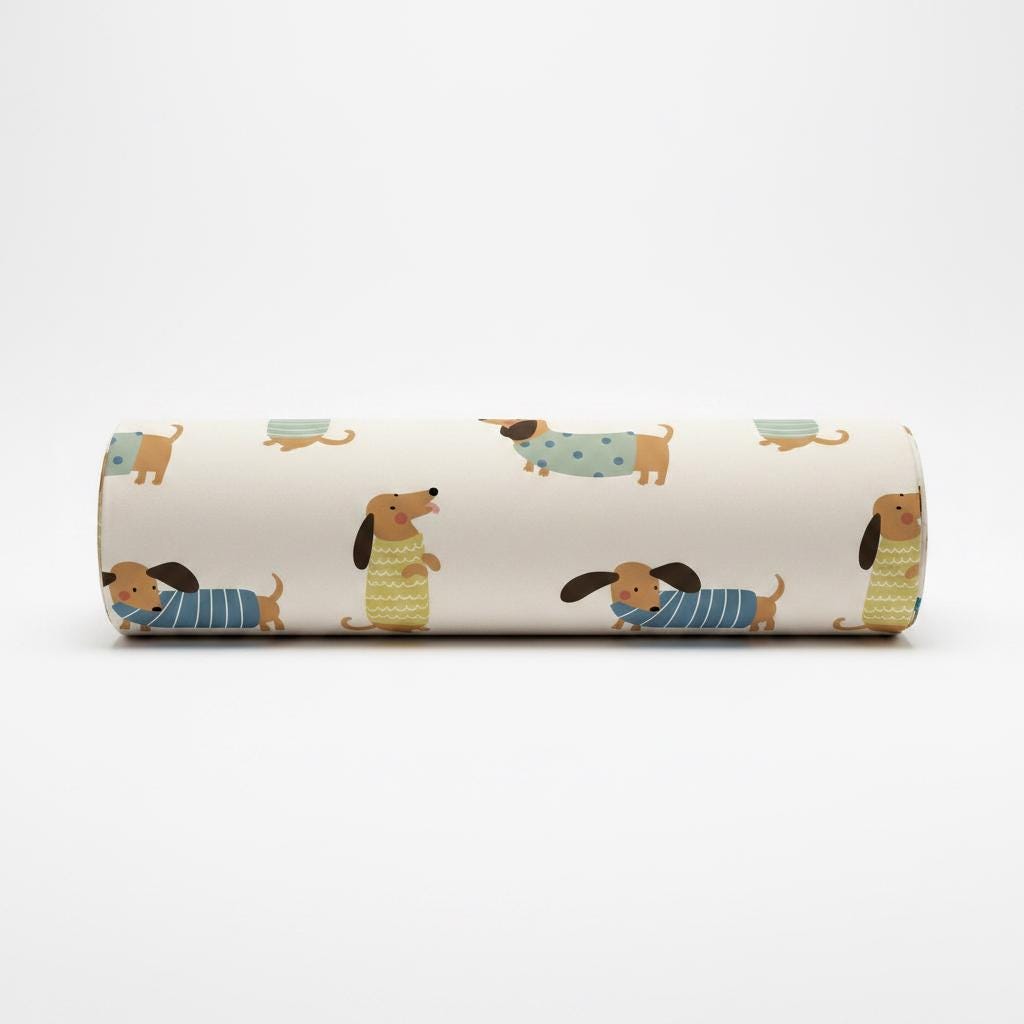 A cylindrical bolster cushion featuring a cream-coloured background with a repeating pattern of brown dachshunds wearing various jumpers and shirts in shades of blue, green, and yellow with polka dot and striped designs.