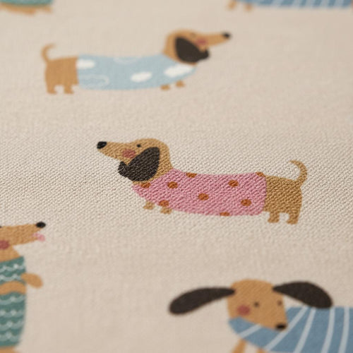 A beige fabric featuring a repeating pattern of brown dachshunds wearing various coloured jumpers. The dogs are depicted in different poses, with some wearing pink polka-dot jumpers, blue cloud-print jumpers, or blue striped jumpers.