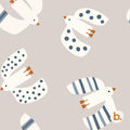 A repeating pattern on a light beige background featuring stylised white birds in flight. The birds have orange beaks and feet, with some wings displaying blue polka dots and others featuring blue vertical stripes. A small logo with the letter b.