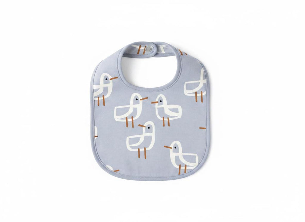 A light blue baby bib featuring a repeating pattern of white seagulls with brown beaks and legs. The bib has a rounded shape with a matching light blue trim around the edges and a single snap closure at the top of the neck opening.