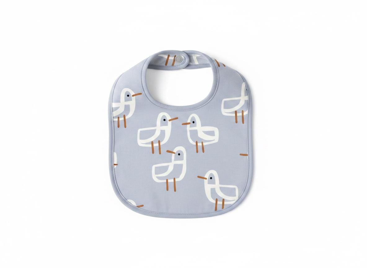 A light blue baby bib featuring a repeating pattern of white seagulls with brown beaks and legs. The bib has a rounded shape with a matching light blue trim around the edges and a single snap closure at the top of the neck opening.