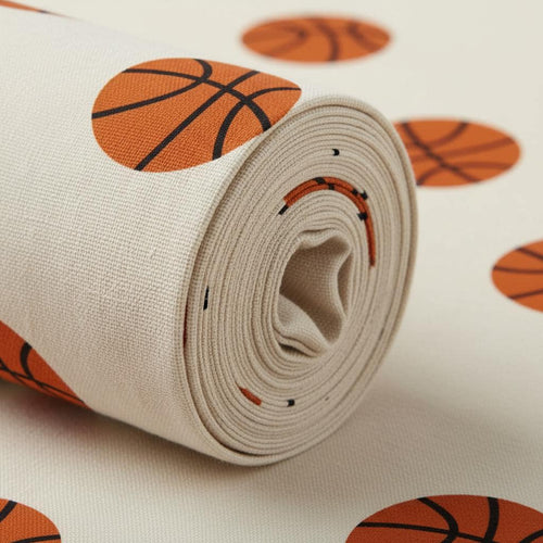 A roll of off-white fabric featuring a repeating pattern of orange basketballs with black lines. The textile has a visible woven texture and is displayed as a partially unrolled cylinder, showing the layered fabric layers.