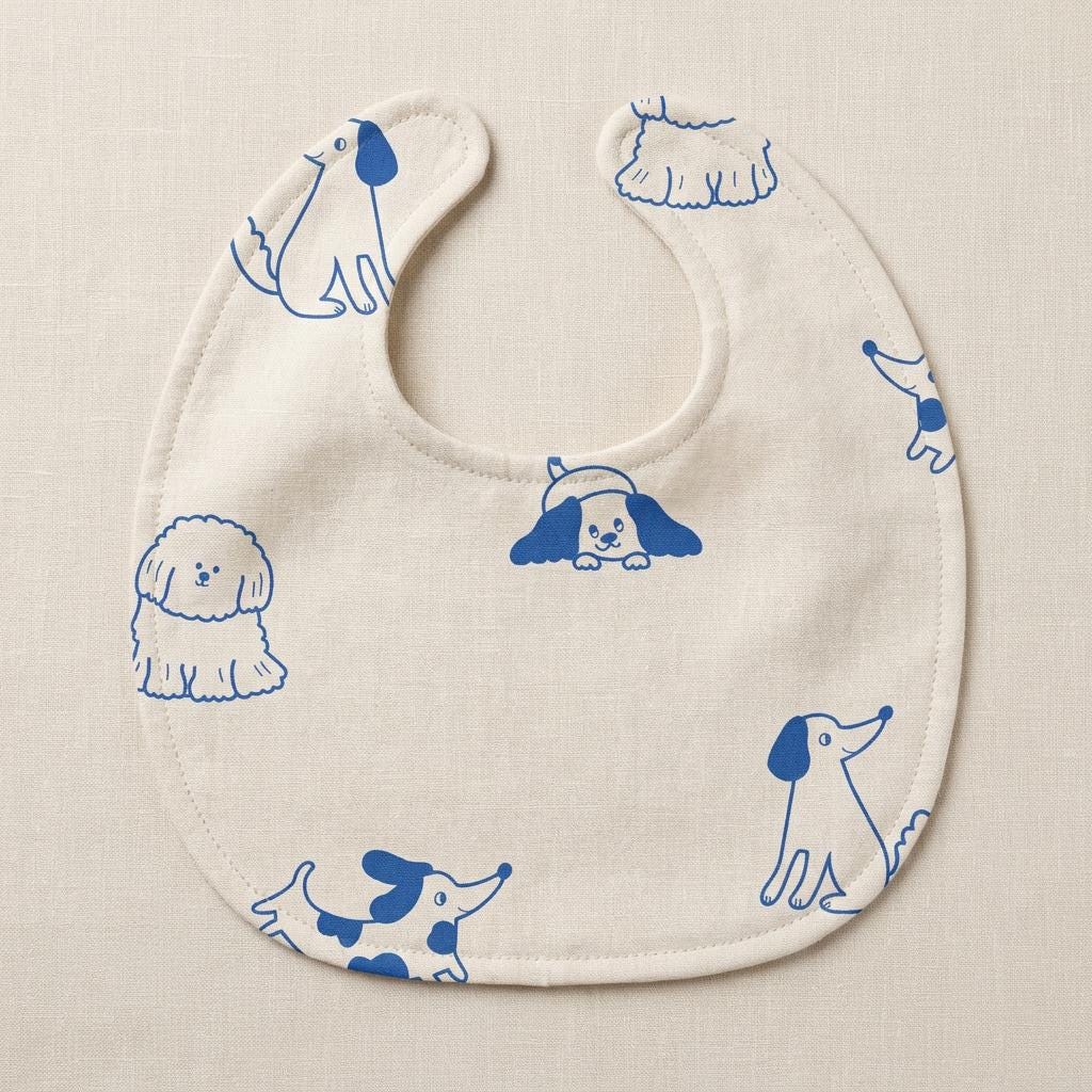 A cream-coloured baby bib featuring a repeating pattern of various dog breeds illustrated in a vibrant blue line art style. The bib has a rounded shape with a central neck opening and finished edges, showcasing different canine poses.