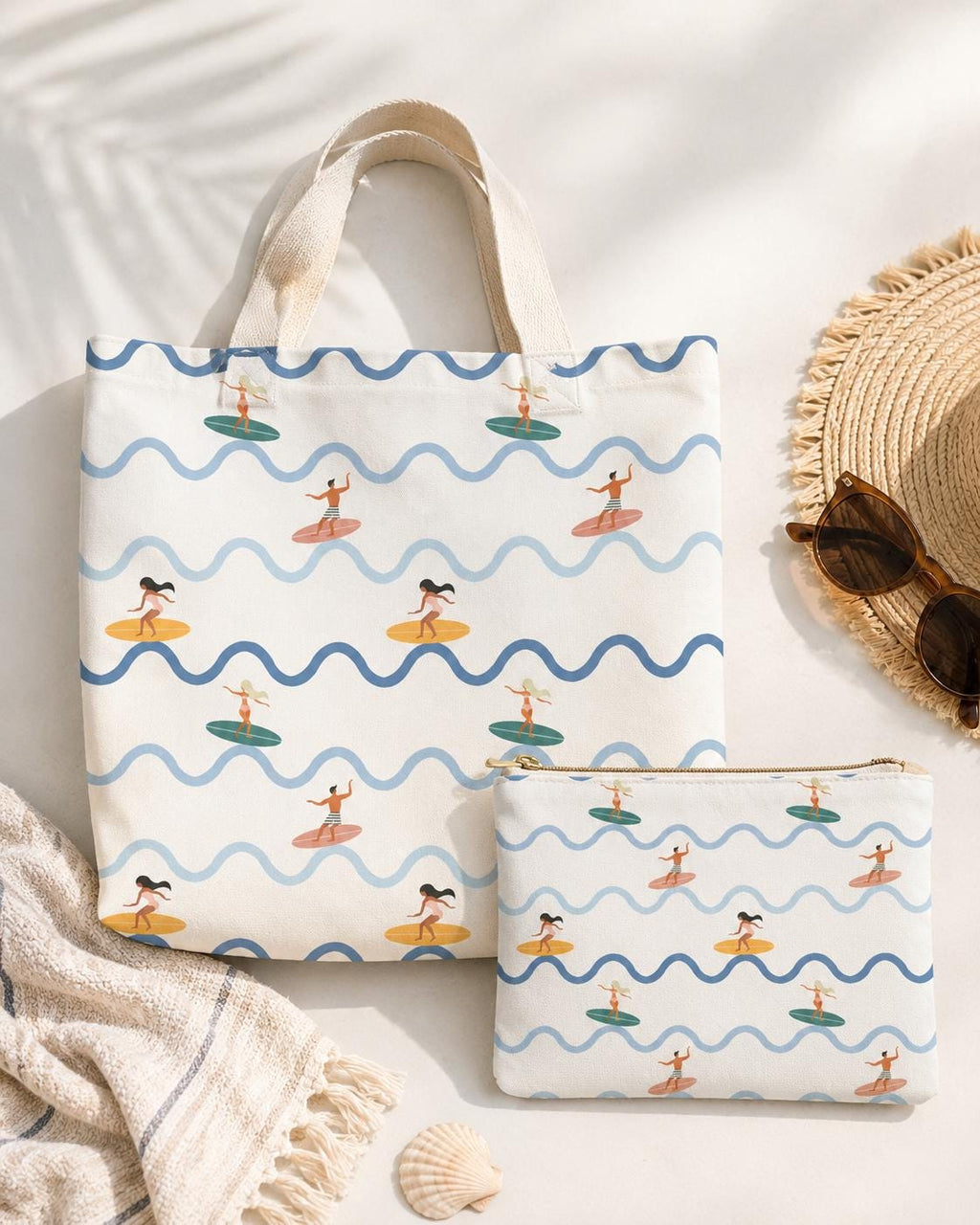 A cream-coloured canvas tote bag and a matching zippered pouch, both featuring a repeating pattern of blue wavy lines and small illustrations of people surfing on colourful surfboards. The bags have sturdy off-white fabric handles.