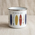 A white enamel mug with a silver rim featuring a colourful graphic print of various surfboards and the text "JUST ADD THE WAVES" in black lettering. The design includes yellow, red, blue, and dark purple surfboard illustrations.