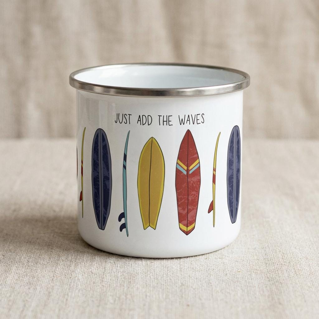 A white enamel mug with a silver rim featuring a colourful graphic print of various surfboards and the text "JUST ADD THE WAVES" in black lettering. The design includes yellow, red, blue, and dark purple surfboard illustrations.
