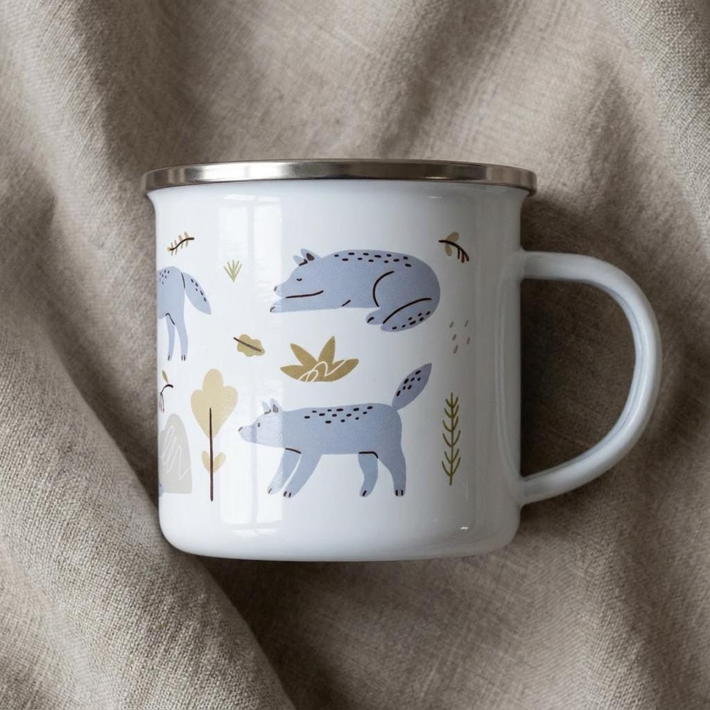 A white enamel mug with a silver-toned rim and handle, featuring a repeating pattern of light blue wolves in various poses, interspersed with small yellow and brown stylised trees and foliage elements across the exterior surface.