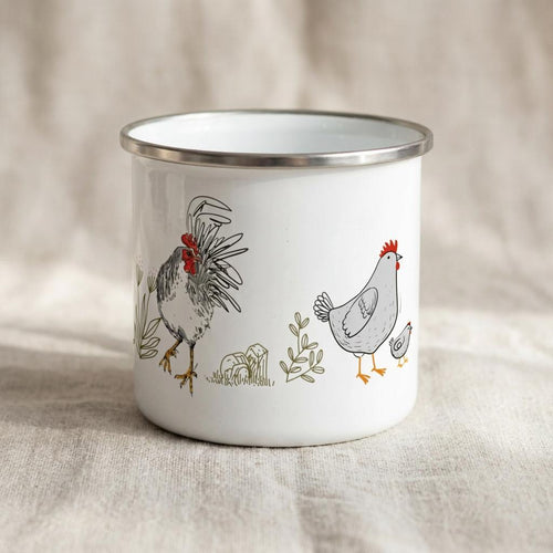 A white enamel mug with a silver-toned rim featuring a black and white line drawing of a rooster, a hen, and a small chick. The illustration includes subtle red accents on the rooster's comb and the hen's comb, along with green foliage.