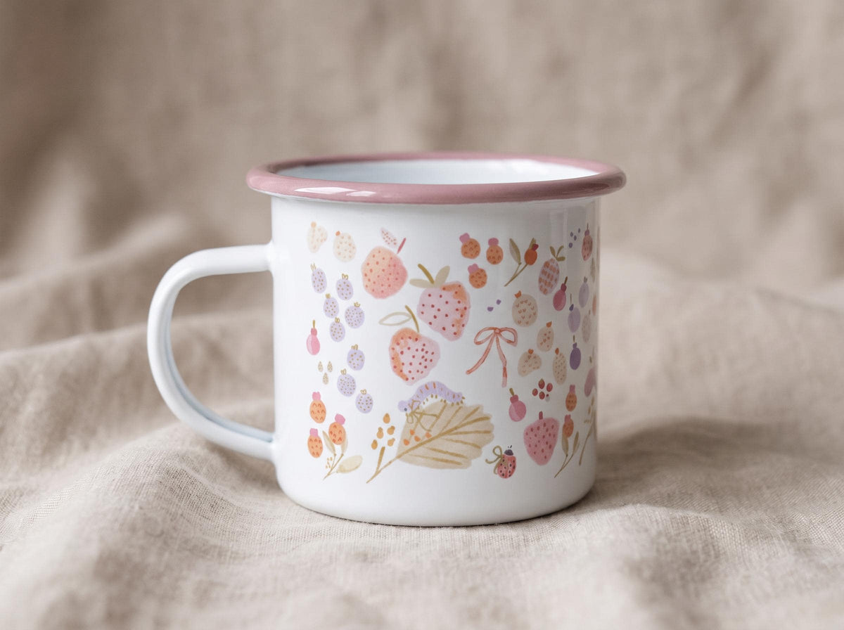 A white enamel mug with a pink rim and handle, featuring a repeating pattern of small illustrations including strawberries, berries, a caterpillar on a leaf, a ladybug, and a ribbon in soft shades of pink, orange, and purple.