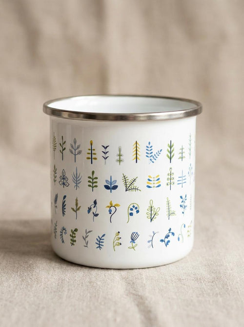 Front view of the Botanical Leaf enamel mug showing neat rows of tiny plant sprigs, ferns and berries in green and blue, on linen.