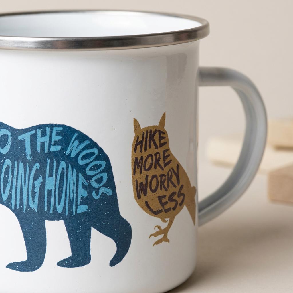 Close-up of the Woodland Animal enamel mug showing the blue bear lettered Going to the woods is going home and the mustard owl lettered Hike more, worry less.