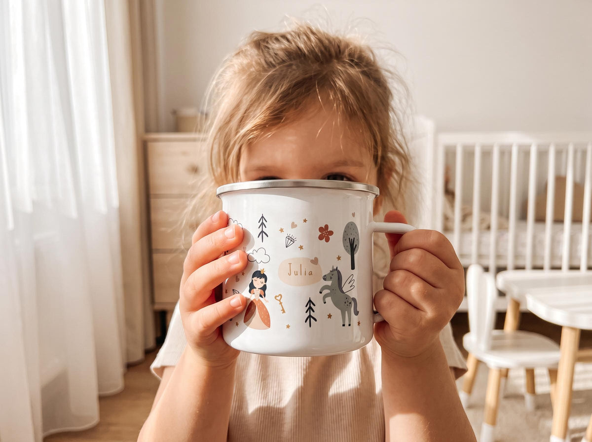 A white enamel mug with a silver rim featuring a colourful graphic print of a princess, a winged horse, trees, flowers, and a diamond. The name Julia is printed in the centre of the design on a light-coloured oval background.