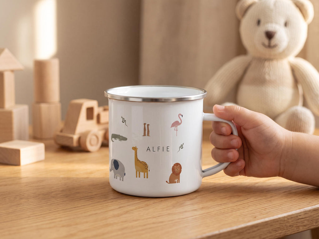 A white enamel mug with a silver rim featuring colourful illustrations of various animals including a giraffe, lion, elephant, and flamingo, with the name ALFIE printed in black text in the centre of the mug surface.
