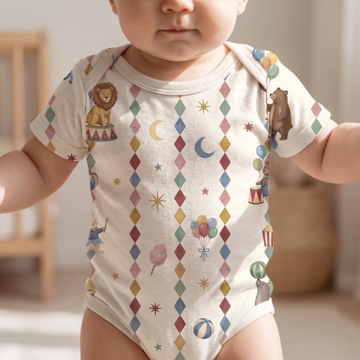 A short-sleeved baby bodysuit in cream featuring a vertical diamond pattern in muted tones of red, blue, green, and yellow. The fabric is decorated with illustrations of circus animals, balloons, stars, moons, and popcorn containers.