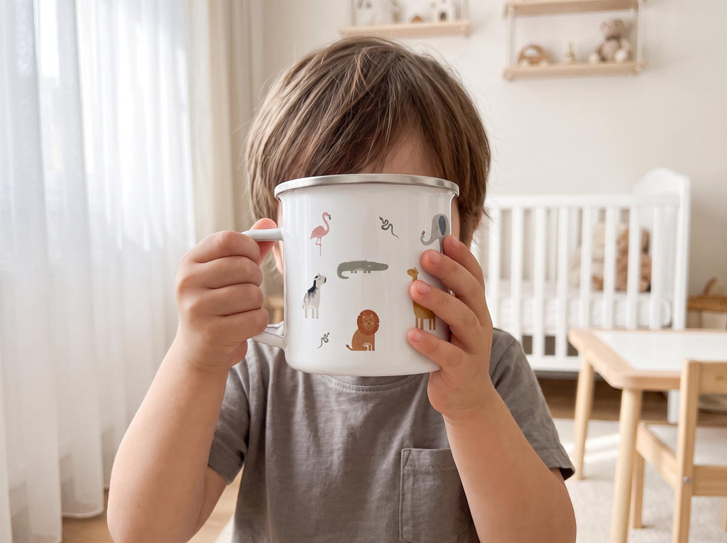 A white enamel mug with a silver rim featuring small, colourful illustrations of various animals including a pink flamingo, a grey elephant, a brown lion, a giraffe, a crocodile, and a snake scattered across the exterior surface.