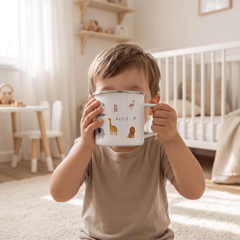 A white enamel mug with a silver rim and handle, featuring colourful illustrations of various animals including a giraffe, elephant, lion, and flamingo, with the name ALFIE printed in black capital letters in the centre.