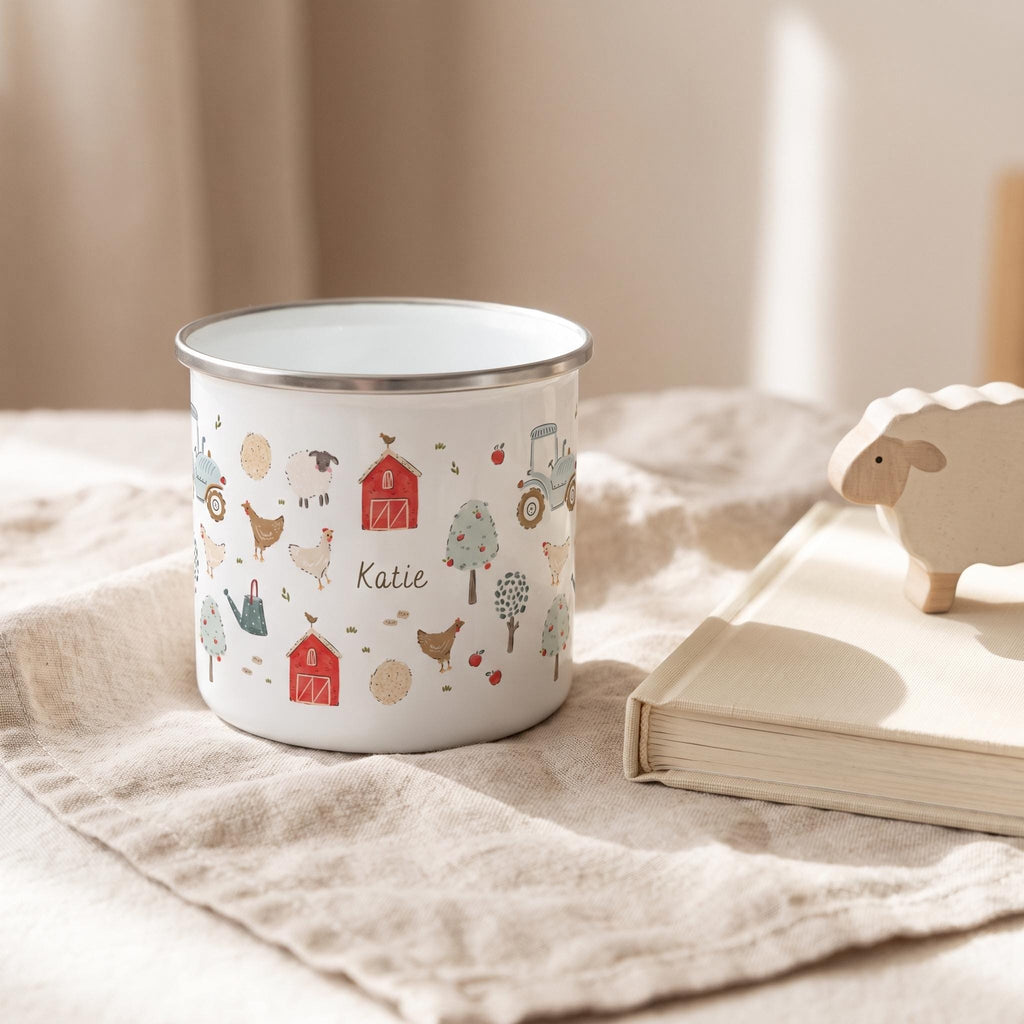 A white enamel mug with a silver rim featuring a colourful farm-themed pattern of red barns, tractors, chickens, sheep, trees, and apples. The name Katie is printed in the centre of the design among the various farm illustrations.