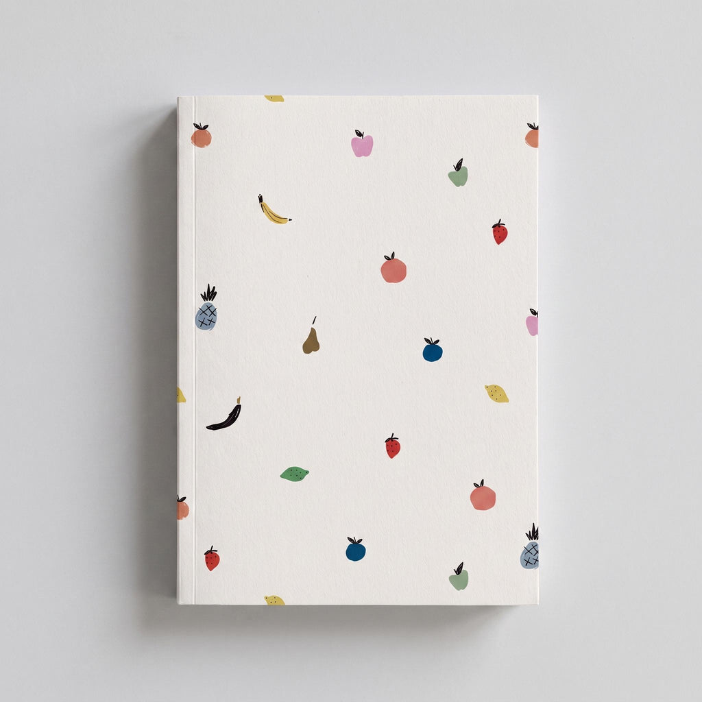 A rectangular notebook with a white cover featuring a repeating pattern of small, hand-drawn style illustrations of various fruits including bananas, pineapples, strawberries, pears, and lemons in muted colours like pink, blue, and yellow.