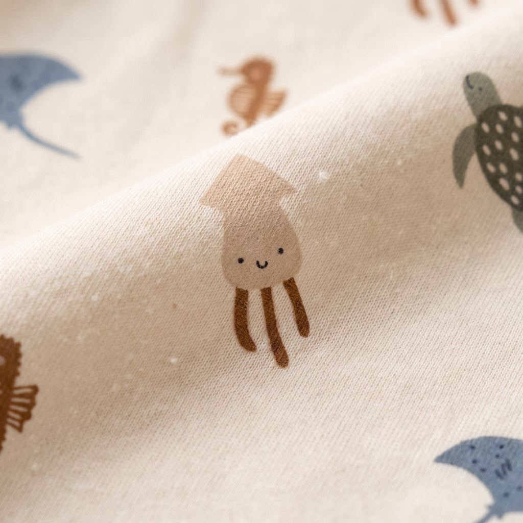 A light beige fabric featuring a repeating pattern of small, simple illustrations of sea creatures including a brown squid, a green sea turtle, a blue stingray, and a brown seahorse, all rendered in a clean, minimalist graphic style.