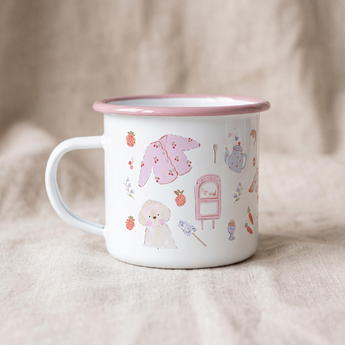 A white enamel mug with a pink rim and handle, featuring a repeating pattern of small illustrations including a pink cardigan, a light brown dog, a pink mailbox, strawberries, carrots, a teapot, and various small floral sprigs.