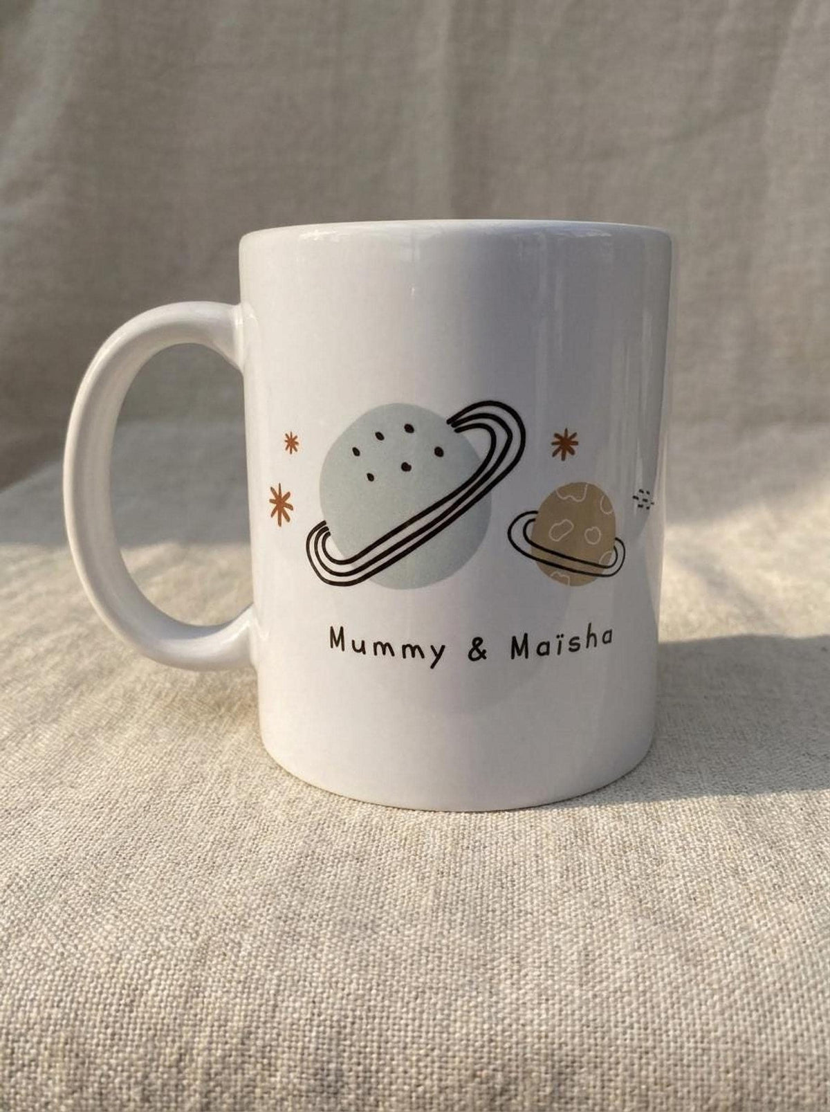 A single large white ceramic mug is printed with illustrations of planets, stars, and the text Mummy & Maisha.