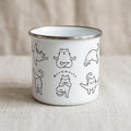 A white enamel camping mug featuring black line drawings of cats in various yoga poses and the text Meowmaste.