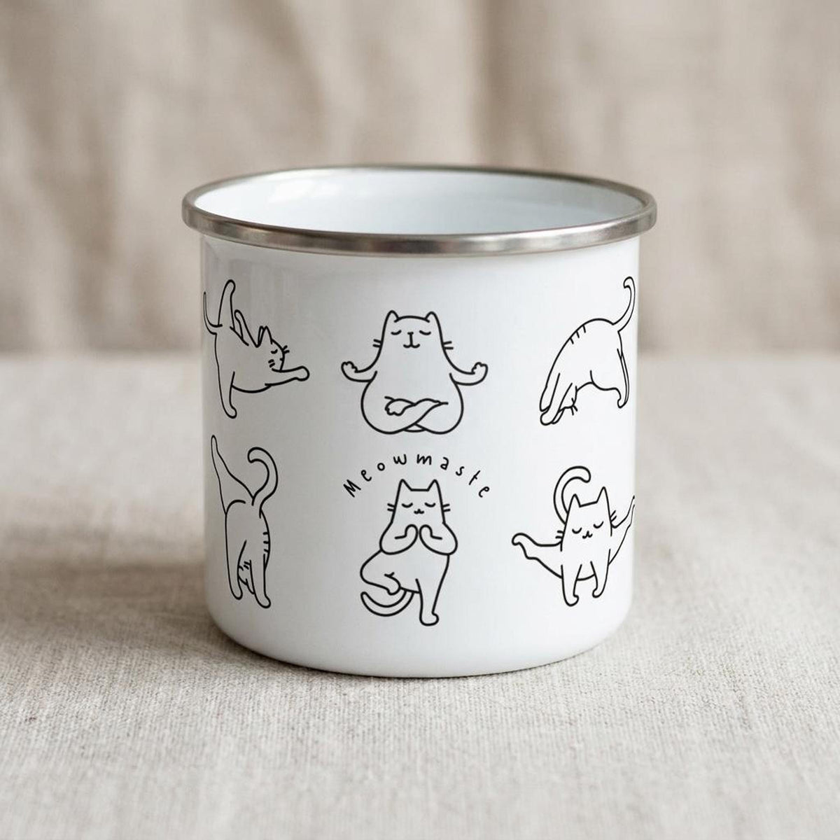 A white enamel camping mug featuring black line drawings of cats in various yoga poses and the text Meowmaste.