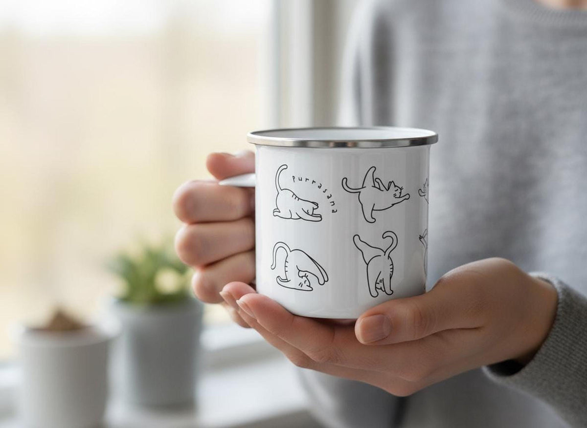 Close-up of hands holding the white enamel mug with cat yoga graphics in front of a window.