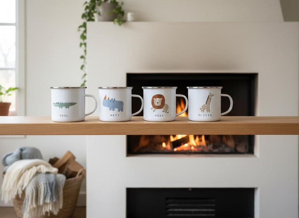 Four white enamel mugs featuring safari animal designs and names lined up on a wooden shelf in front of a fireplace.