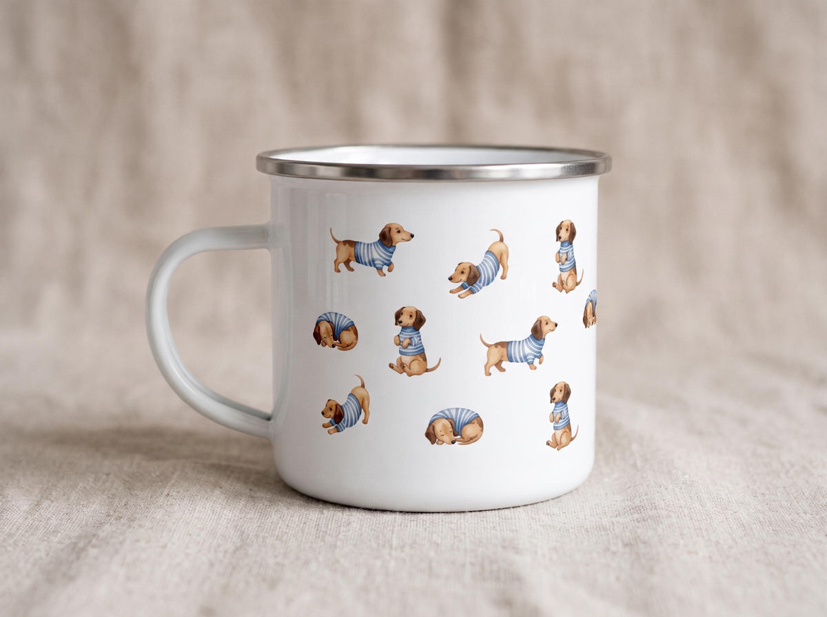 A white enamel camping mug featuring patterns of cartoon dachshunds wearing blue-and-white striped sweaters sits on a light beige textured fabric background.