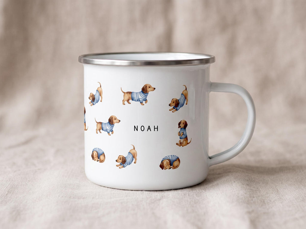 A white enamel mug featuring a pattern of dachshunds in striped sweaters and the name Noah printed in the center stands on a neutral backdrop.