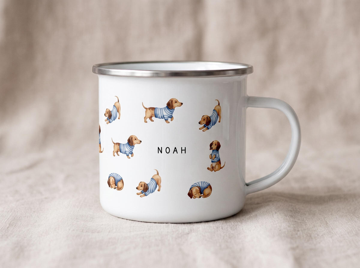 A white enamel mug featuring a pattern of dachshunds in striped sweaters and the name Noah printed in the center stands on a neutral backdrop.