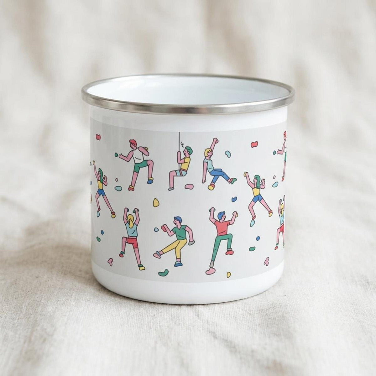A white enamel mug with a silver rim displaying a repeating pattern of colorful rock climbers on a light grey background.