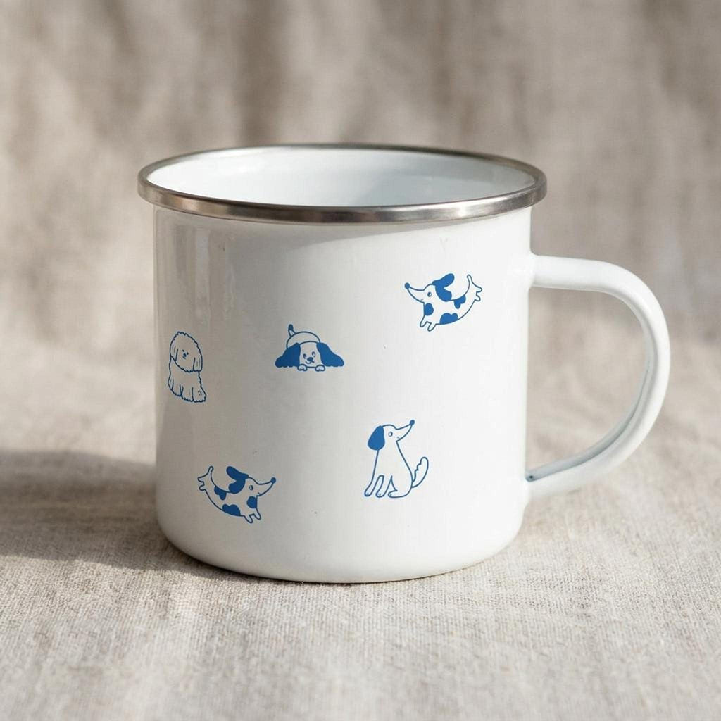 A white enamel mug with a silver rim and blue dog illustrations is angled to show its handle on the right side.