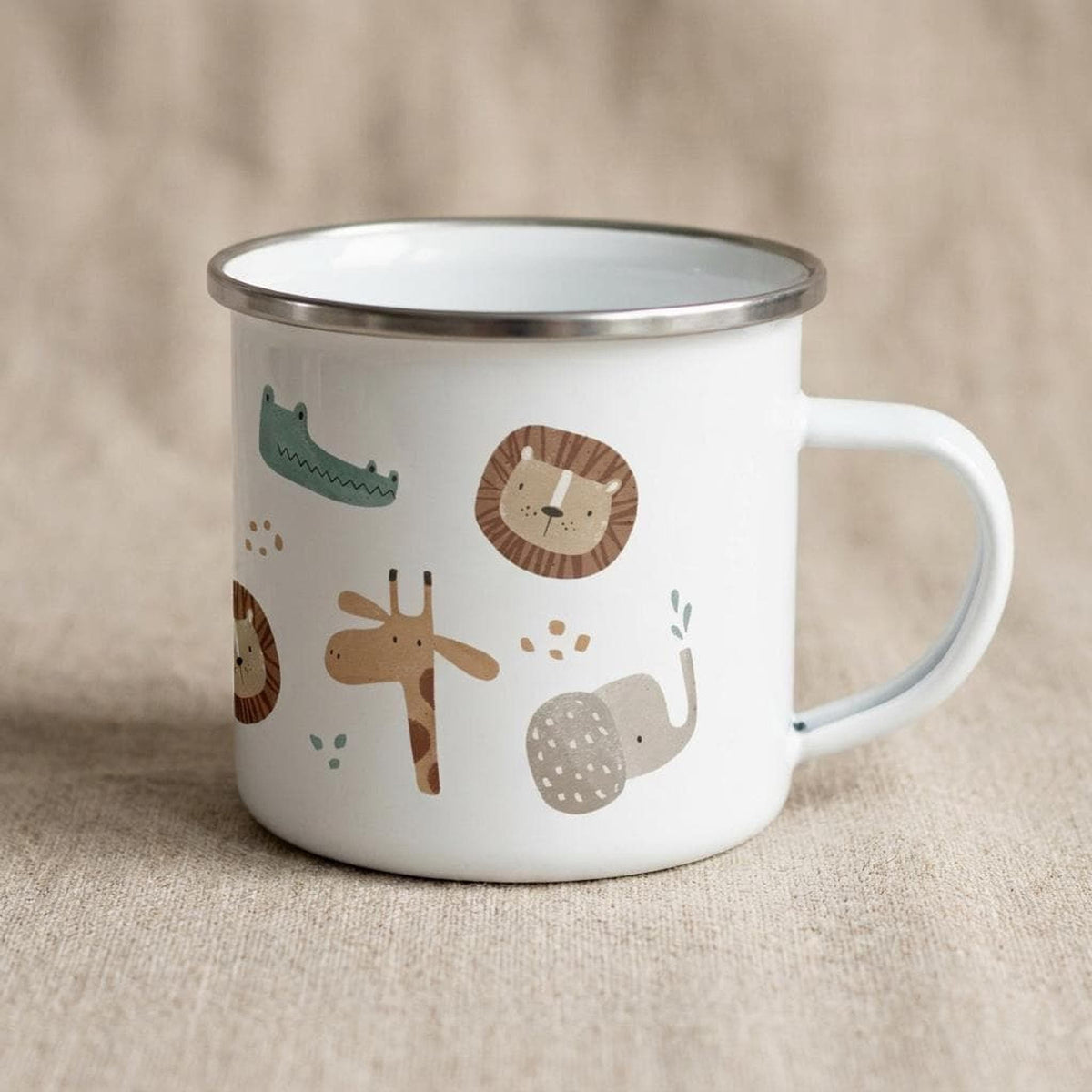 A white metal mug featuring cartoon safari animal graphics sits on a neutral fabric background, viewed from the side with the handle on the right.