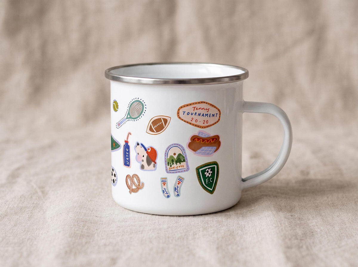 A white enamel mug with a silver rim, showcasing a collection of stickers including football, tennis, and a Tenny Tournament graphic.