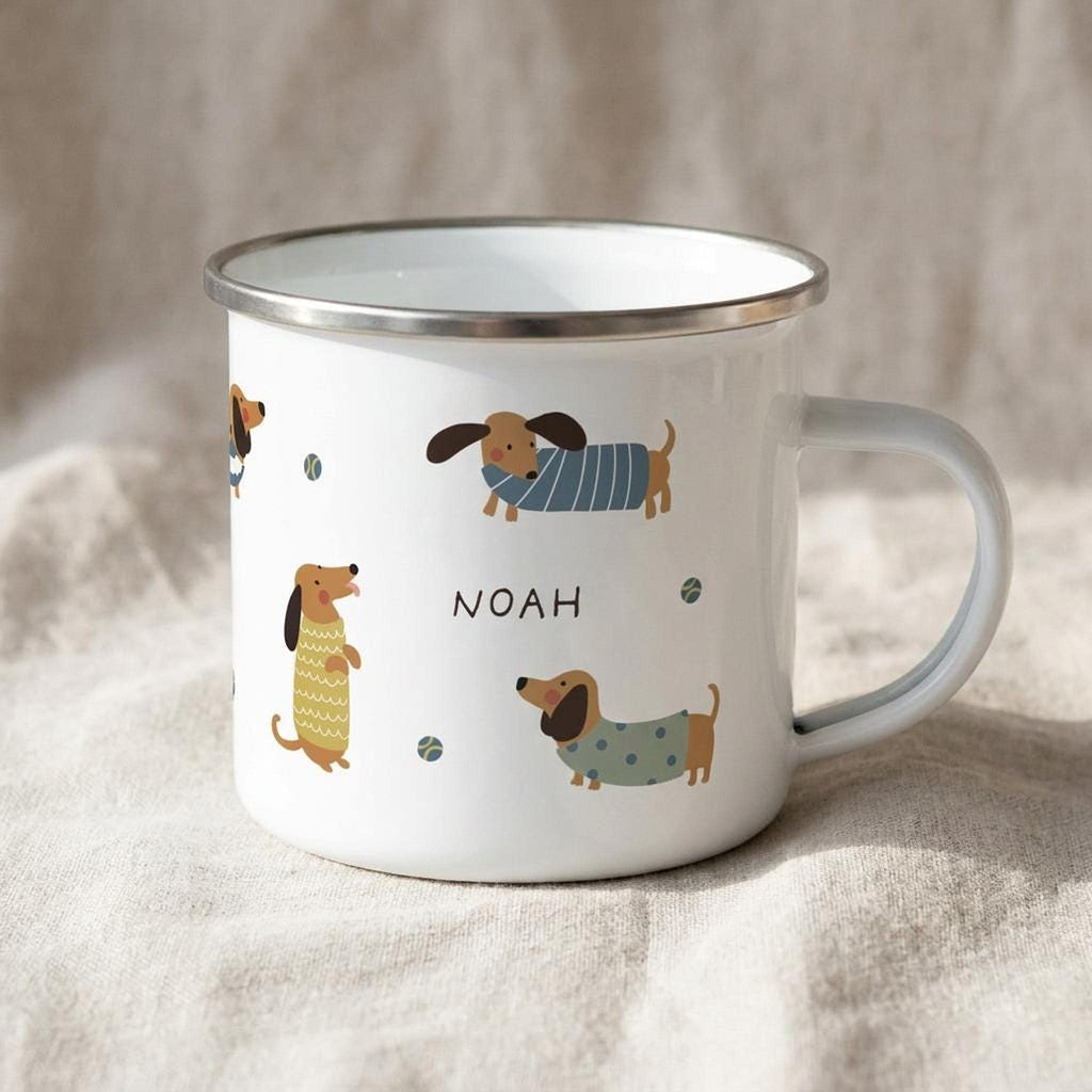 A white enamel mug featuring a pattern of dachshund dogs in sweaters and small balls, with the name Noah printed in the center.