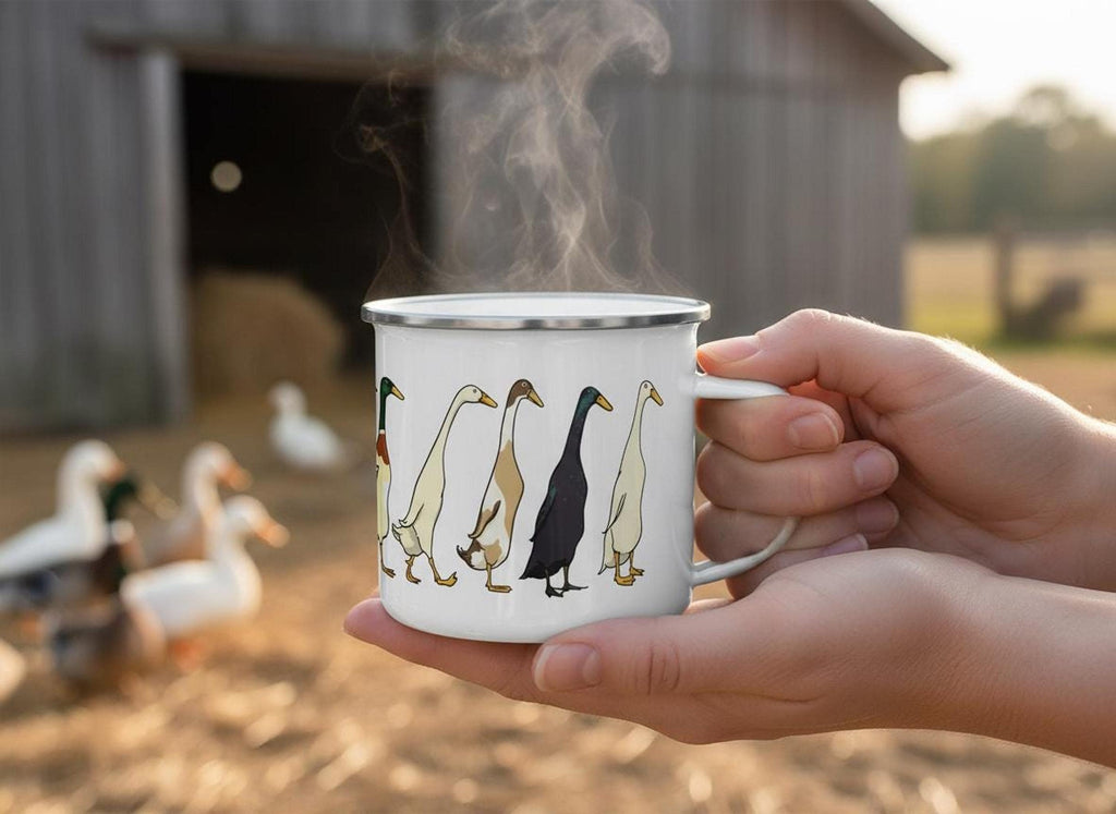 Two hands hold a steaming white enamel mug with a duck illustration, with ducks and a rustic barn visible in a blurred background.