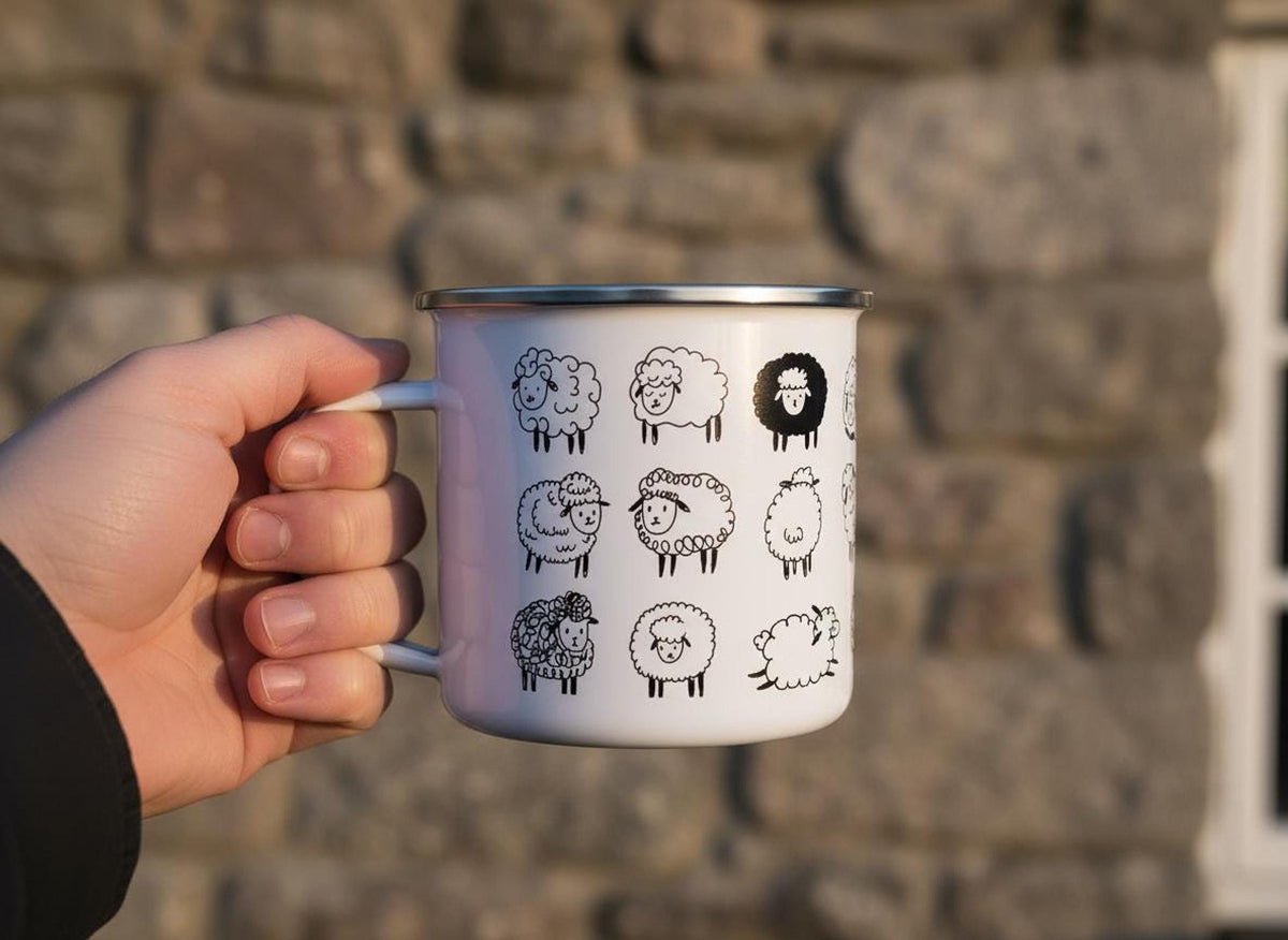 A hand holds a white enamel mug featuring a pattern of black sheep illustrations against a stone wall background.