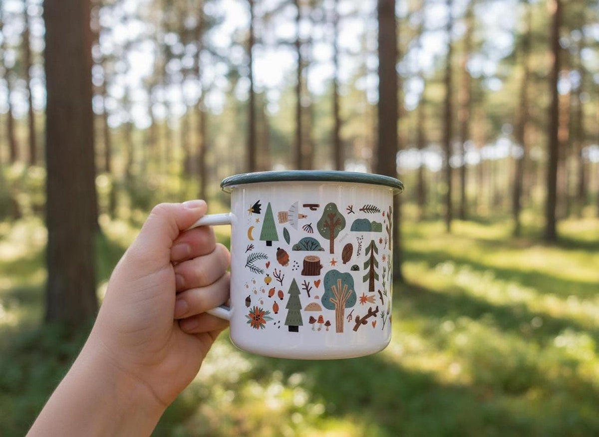 A hand holds a white enamel mug with a green rim against a blurred forest background.